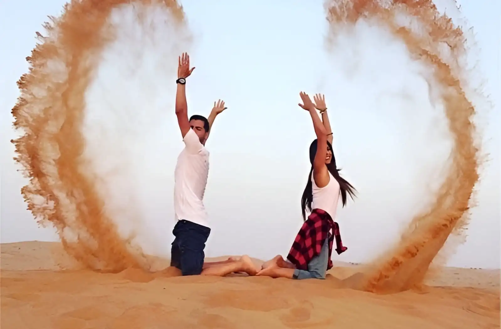 Couple sitting on golden desert dunes and tossing sand into the air during a premium desert safari in Dubai.