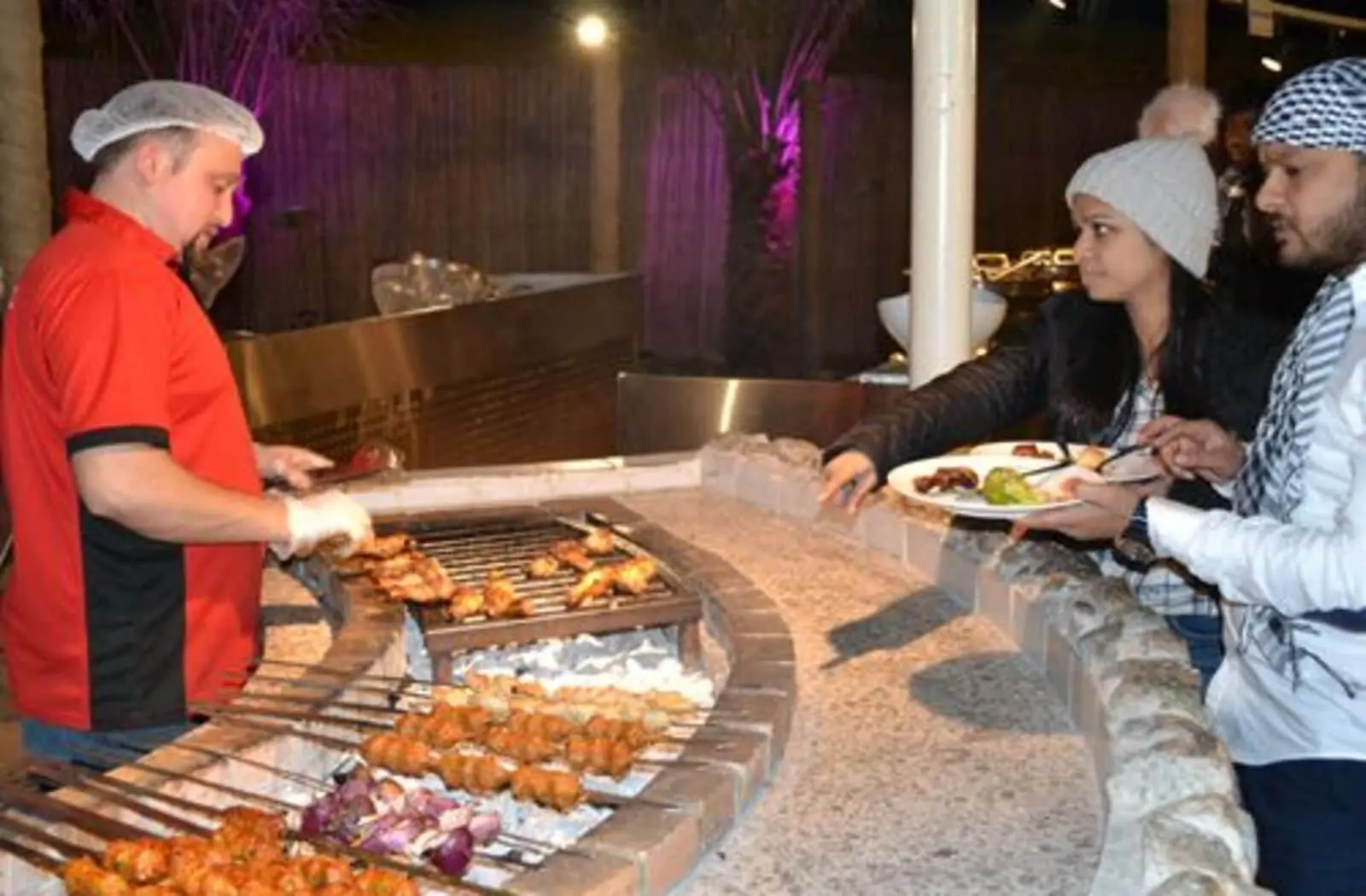 Guests enjoying freshly grilled BBQ from a live cooking station during an evening desert safari in Dubai.