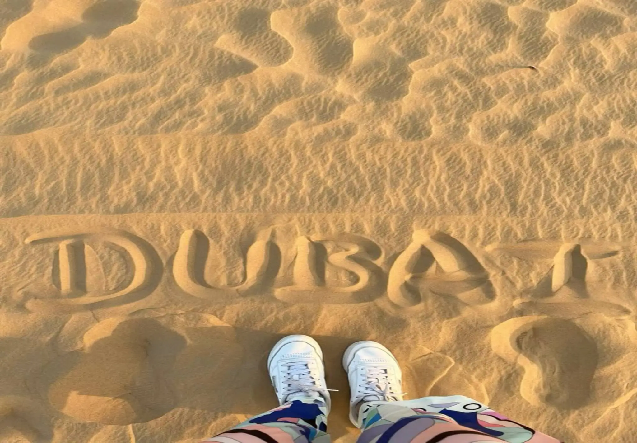 Guest capturing a photo of the Dubai name written on sand during a morning desert safari