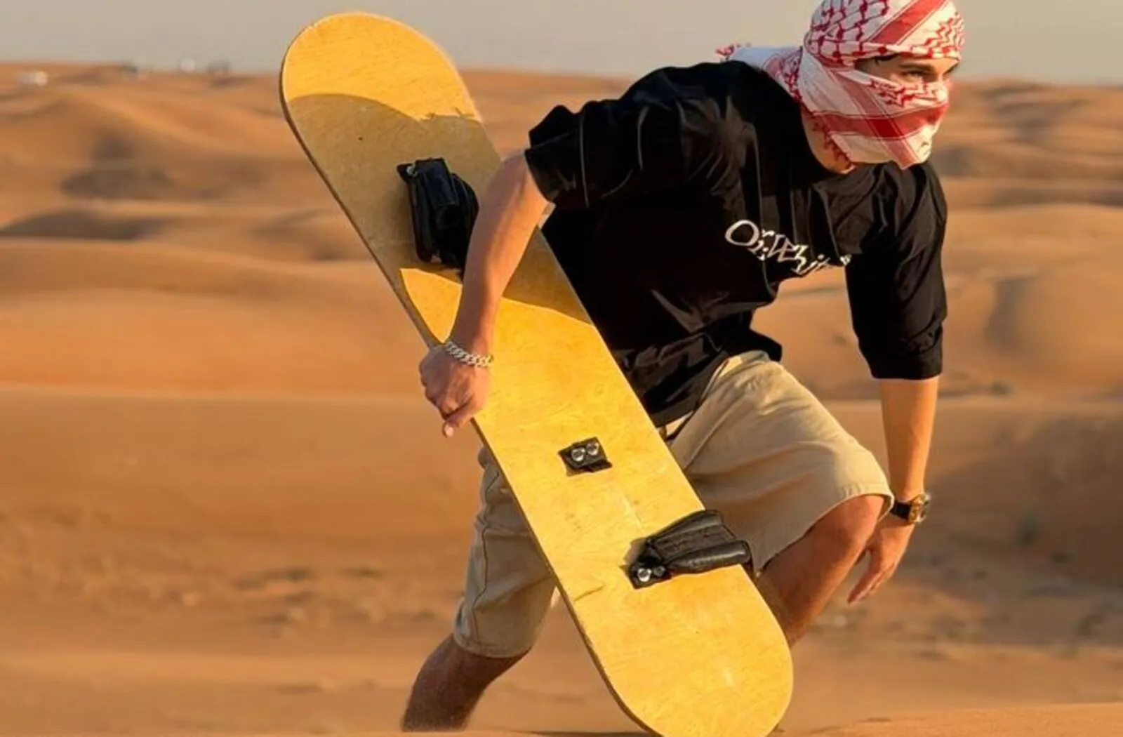 Tourist running across the sand dunes for sandboarding during a desert safari in Dubai
